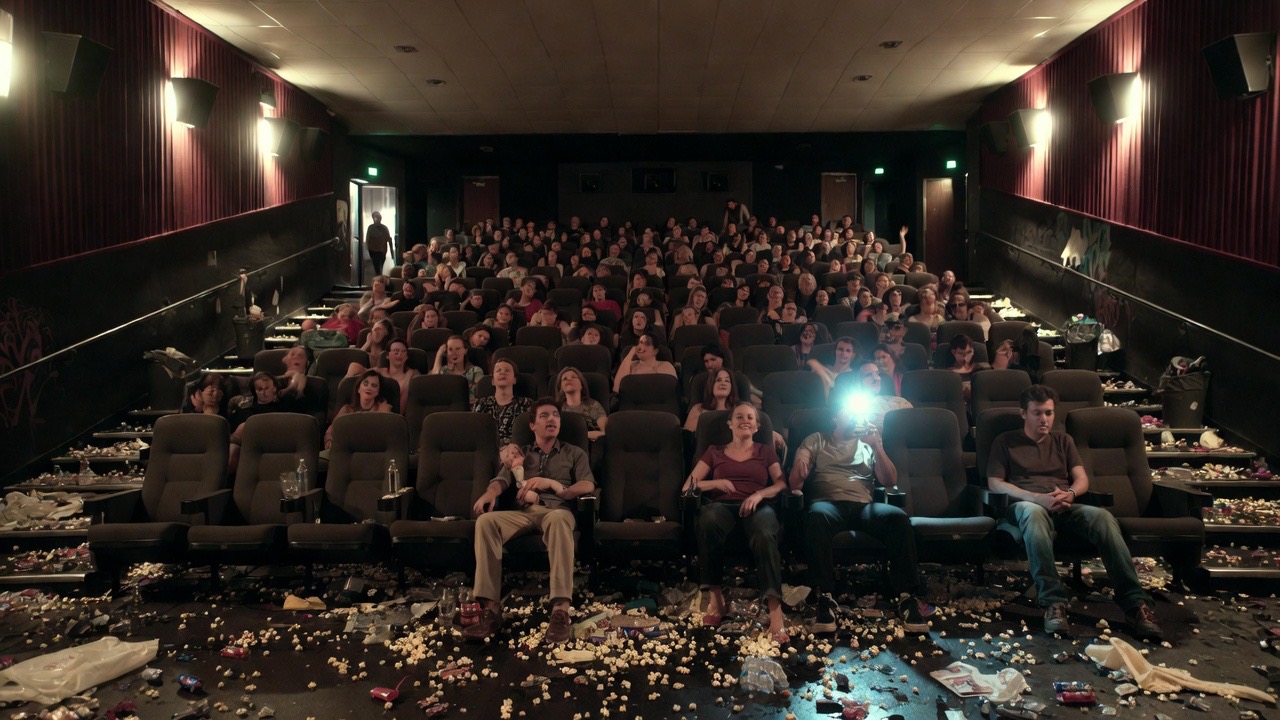 Dark movie theater auditorium with glowing cell phone screens from audience members during a film, empty popcorn buckets scattered, illustrating distractions and poor experience